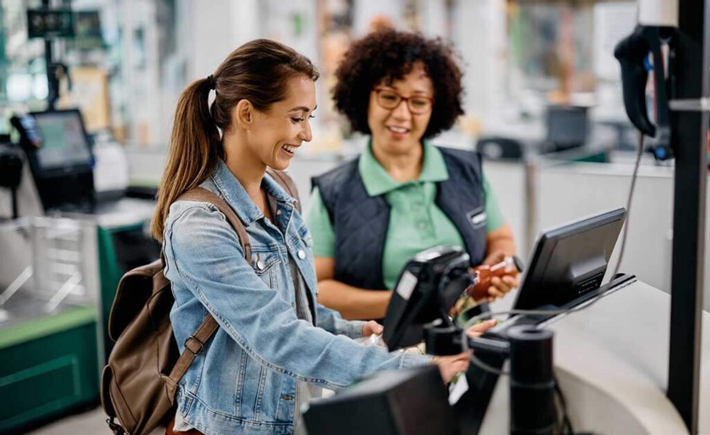 imagem de uma moça pagando uma compra e uma atendente ao lado sorrindo