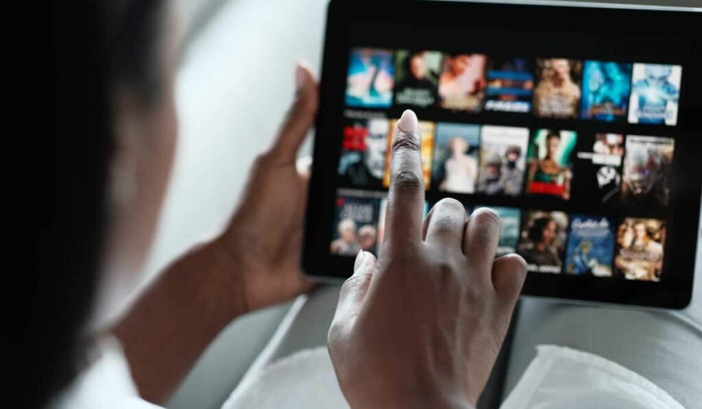 Mão segurando um tablet com o dedo apontando para aplicativo da netflix